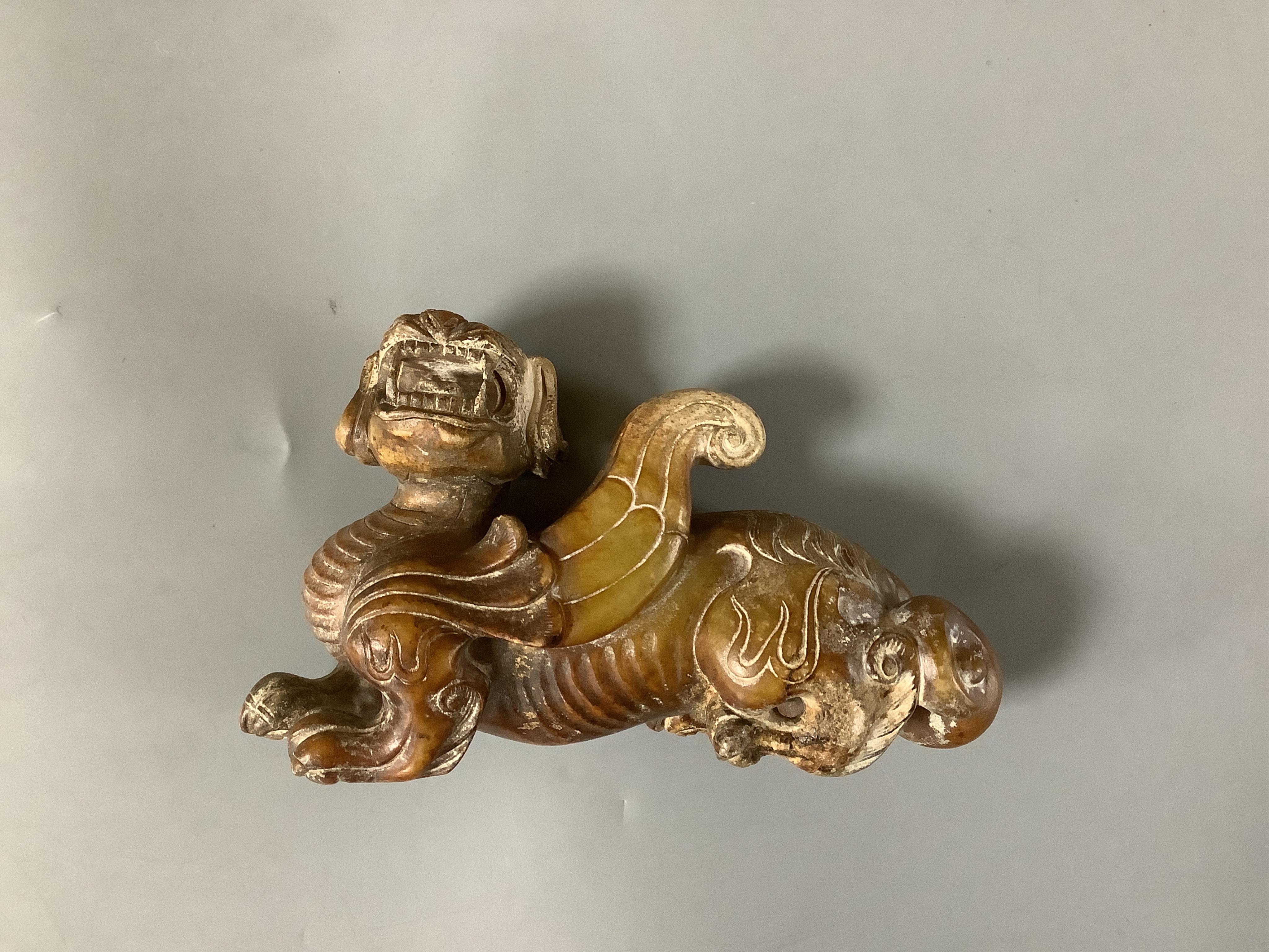 A Chinese archaistic pale celadon russet and burnt jade figure of a winged mythical beast, wood stand, mythical beast 12cm wide. Condition - carving good, stand good